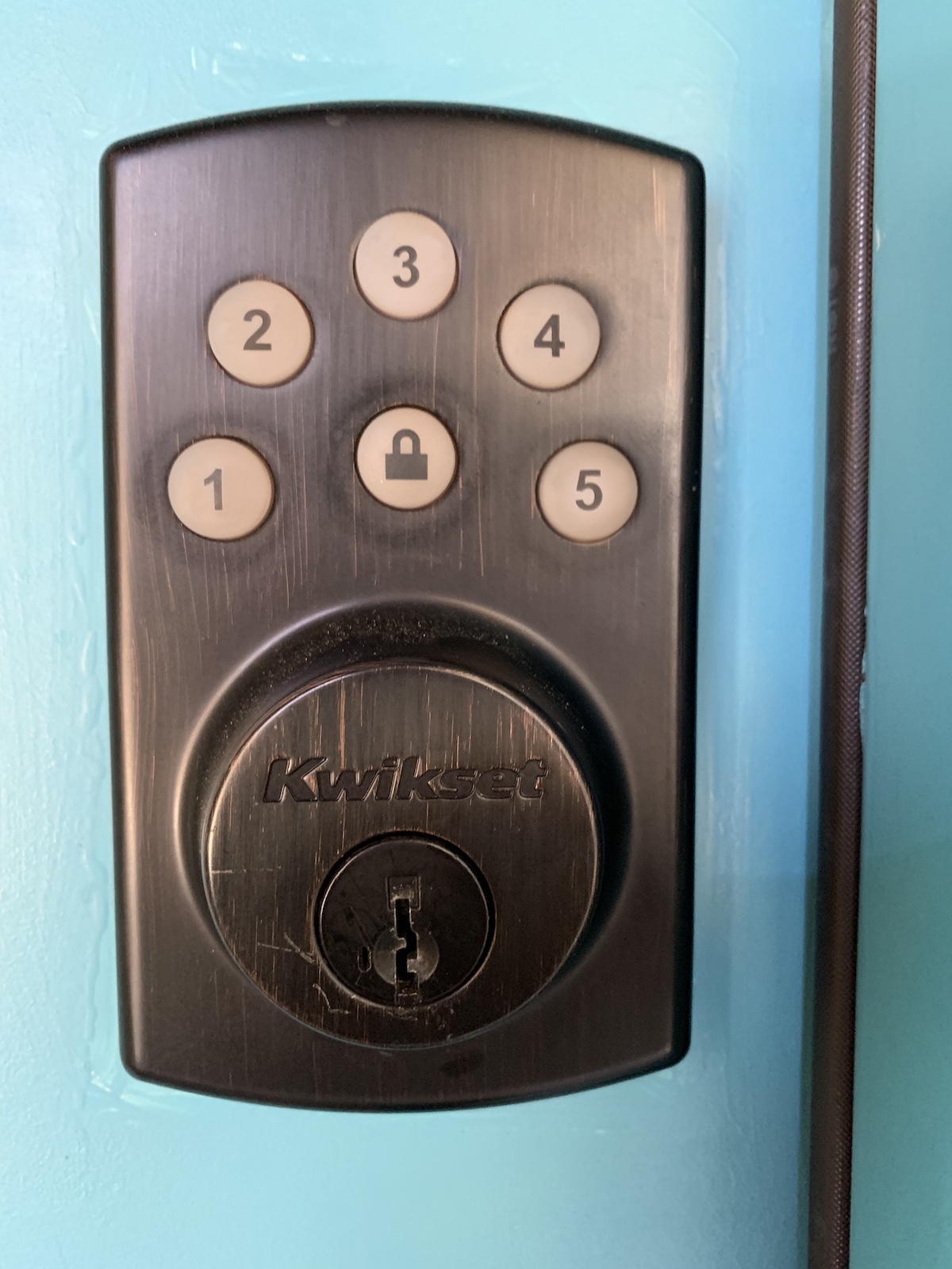 Photo of a keypad-controlled door lock that has five keys labeled 1/2 3/4 5/6 7/8 9/0 and another key having a lock icon.